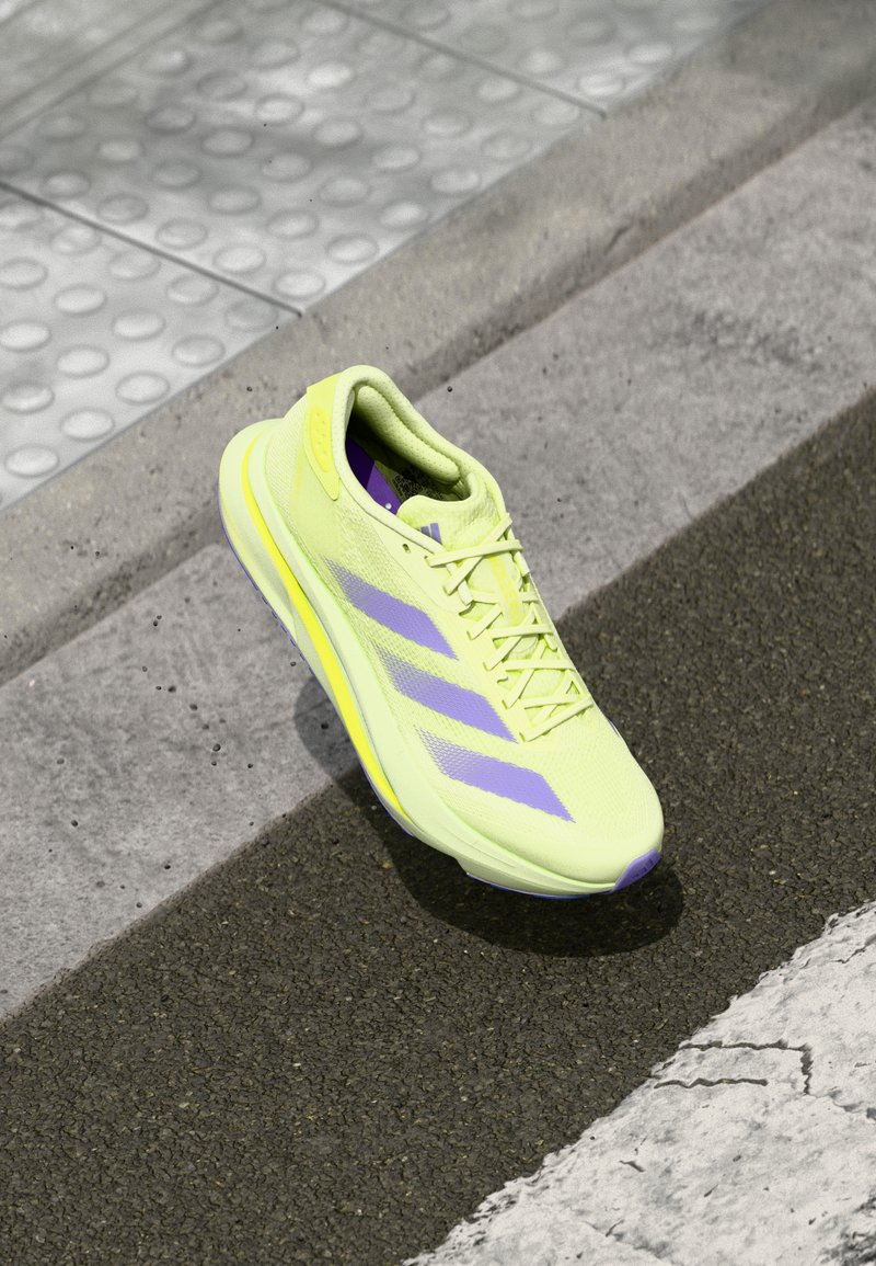 Sneaker verde lime con accenti viola, superiore sintetico leggero, punta rotonda, lacci prominenti e suola testurizzata.