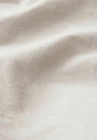 Tessuto beige chiaro con una texture morbida, che mostra lievi pieghe e un motivo di tessitura uniforme. Nessun motivo o accento visibile.