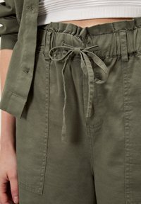 Pantalones verde oliva con cintura ajustable, bolsillos laterales y un corte holgado, confeccionados en una tela suave y con textura.