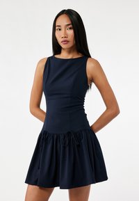 Navy blue sleeveless dress with a fitted bodice and flared skirt. Features a drawstring detail at the waist and smooth, stretchy fabric.