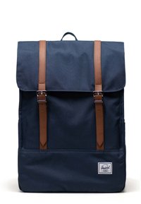 Navy fabric backpack with brown leather straps, top flap closure, rectangular shape, front patch logo, textured surface.