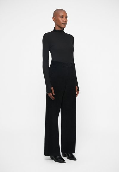 Black turtleneck top and high-waisted black corduroy wide-leg pants, featuring a textured finish and subtle front pleats. Black heeled shoes.