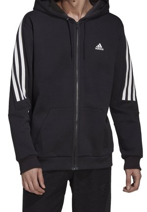 Felpa nera con zip realizzata in un tessuto morbido, dotata di cappuccio con lacci, tasche frontali e tre strisce bianche lungo ogni manica.