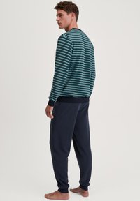 Gestreiftes Langarmshirt in Blau und Grün mit Rundhalsausschnitt, kombiniert mit navyblauen, elastischen, schmal geschnittenen Sweatpants. Weicher Stoff.