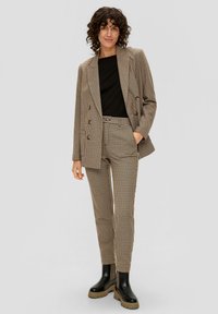 Bruin geblokt colbert en bijpassende broek van textiel, gecombineerd met een zwart top en zwarte enkellaarsjes met grove zolen.
