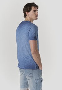 Blaues T-Shirt mit Rundhalsausschnitt und kurzen Ärmeln, mit einem Farbverlauf-Design und umgeschlagenen Bündchen. Leichter Stoff mit glatter Textur.