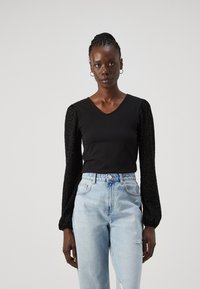 Svart V-hals topp med teksturert, puffet leopardmønster på ermene; kombinert med lyseblå høytlivede, slitte jeans.