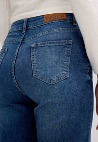 Jeans de mezclilla azul oscuro con una textura suave, bolsillos traseros y una etiqueta de cuero marrón que dice "INSIDE" en la cintura.