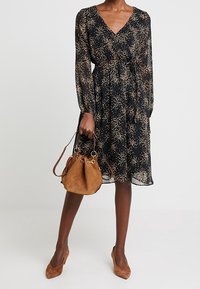 Svart klänning med V-ringning, långa ärmar och spridda guldprickar. Kombineras med en brun mockaväska och matchande klackar.