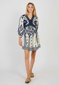 Korte mouwen jurk in crème en marineblauw, met geometrische patronen, een v-halslijn en een empire taille met een uitlopende rok.