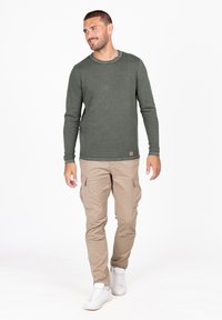 Langärmliges olivgrünes, geripptes Shirt mit rundem Halsausschnitt, kombiniert mit beigen Cargo-Hosen und weißen Sneakers.