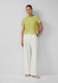 Limonkowa bluzka z koronką w kropki z falbaniastym dołem, połączona z białymi, luźnymi spodniami i sandałami na obcasie z paskami.