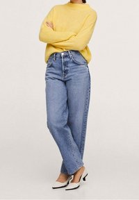 Helles gelbes Strickpullover, lässige blaue Jeans mit hoher Taille und weiße Schuhe mit schwarzen Akzenten. Glatte Textur, lässiges Design.