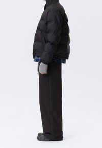 Chaqueta negra acolchada con cuello alto, combinada con una camisa de cuadros azul y guantes sin dedos grises. Pantalones negros holgados y zapatos oscuros.