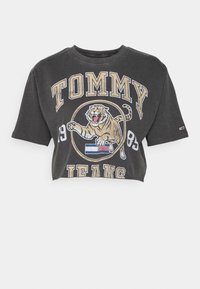 Zkrácený šedý tričko vyrobené z bavlny, s grafikou tygra a textem "TOMMY JEANS 1985" v žluté a bílé barvě. Kulatý výstřih a krátké rukávy.