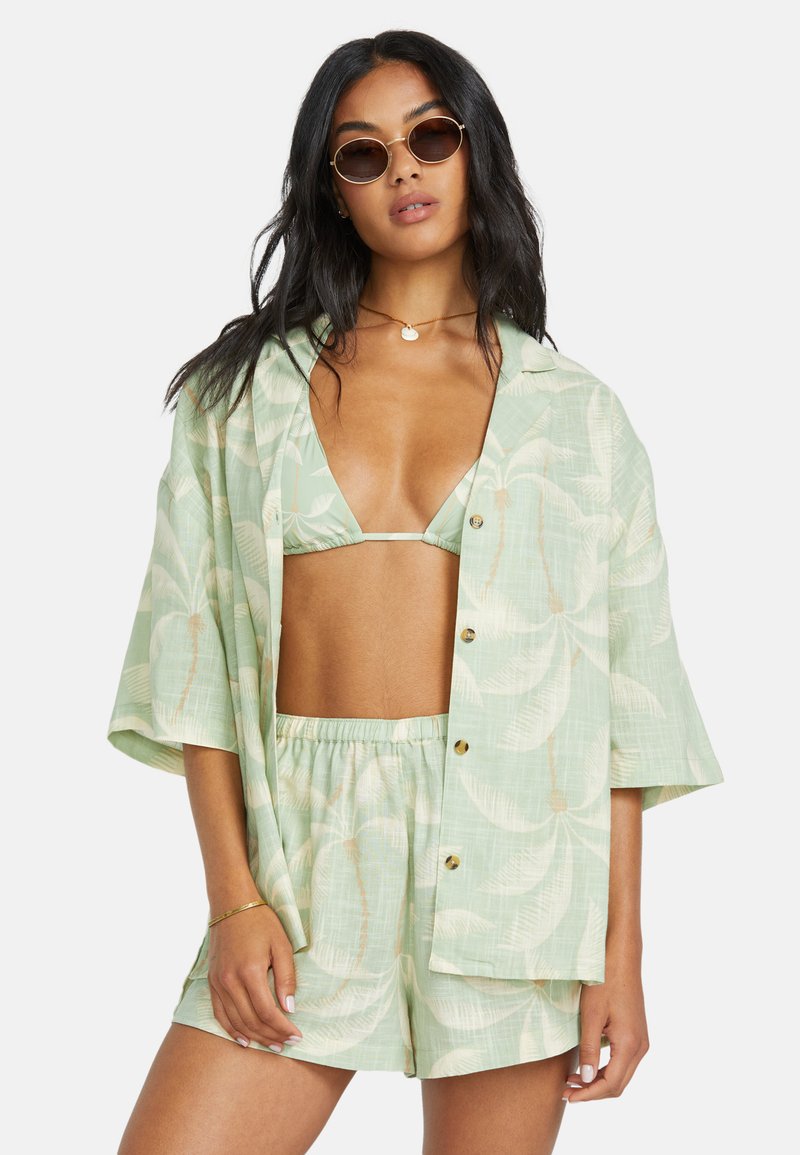 Completo da resort verde chiaro composto da una camicia corta a maniche corte con bottoni, pantaloni corti abbinati e un top bikini con un motivo di foglie.