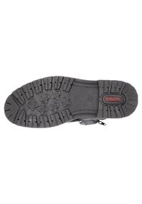 Suela de zapato de goma negra con surcos y ranuras profundas, que presenta patrones en forma de estrella para mayor tracción y un destacado logotipo de marca rojo.