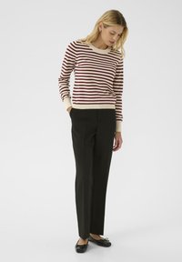 Pull rayé rouge et crème avec un col et des poignets côtelés, associé à un pantalon droit noir et des chaussures plates noires.