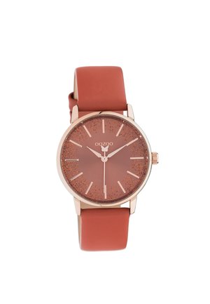 Montre analogique en or rose avec un cadran rond en bronze pailleté, des index horaires minimalistes et un bracelet en silicone terracotta lisse.