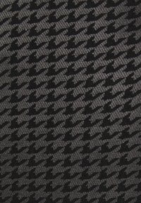 Texturerad tyg med ett hundtandsmönster i varierande nyanser av svart och grått, som förmedlar en sofistikerad design med en matt yta.