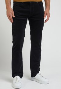 Svarta kordbyxor med slim fit, fem fickor och bältesloopar, tillsammans med vita sneakers. Texturerat tyg med synlig ribbning.