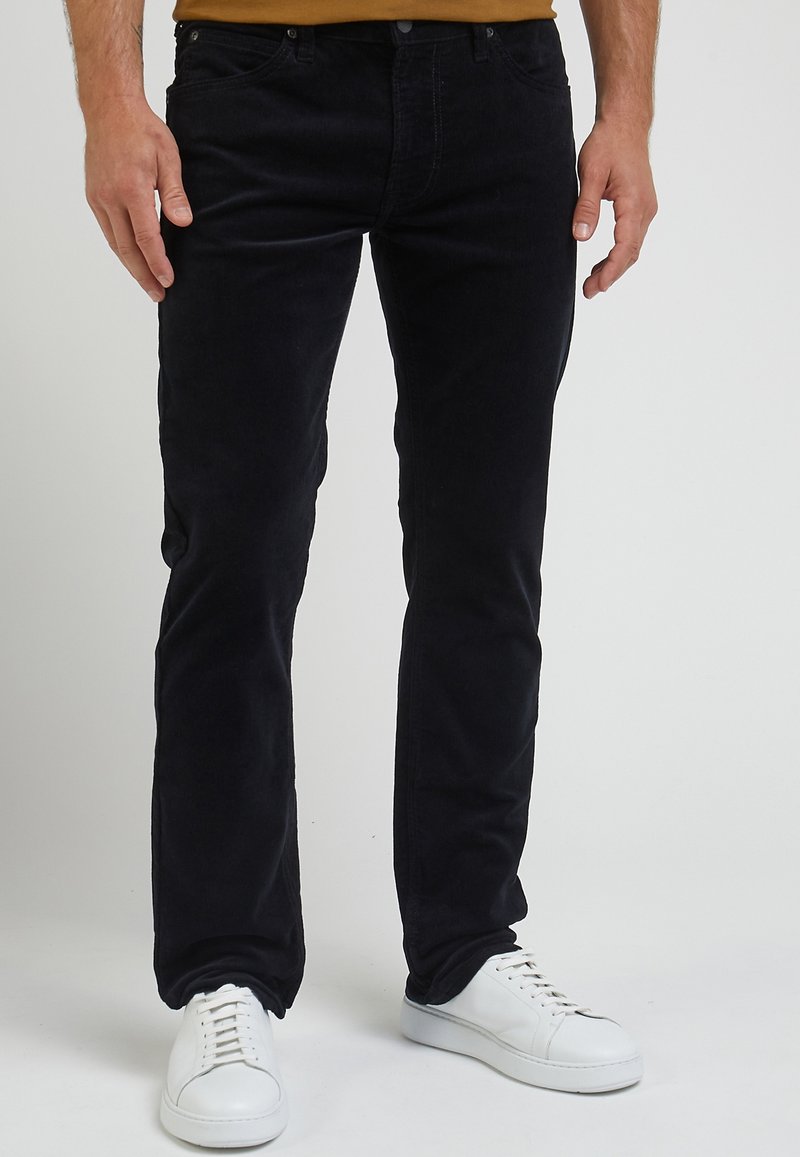 Svarta kordbyxor med slim fit, fem fickor och bältesloopar, tillsammans med vita sneakers. Texturerat tyg med synlig ribbning.