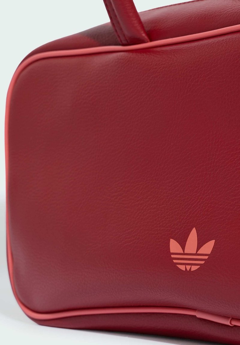Borsa rettangolare in pelle rossa con angoli arrotondati, manico sulla parte superiore e piccolo logo Adidas trefoil nell'angolo in basso a destra.