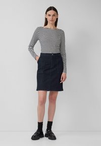 Un haut à manches longues rayé en noir et blanc, associé à une jupe crayon en denim foncé avec poches avant et fermeture par bouton, portée avec des chaussures noires.