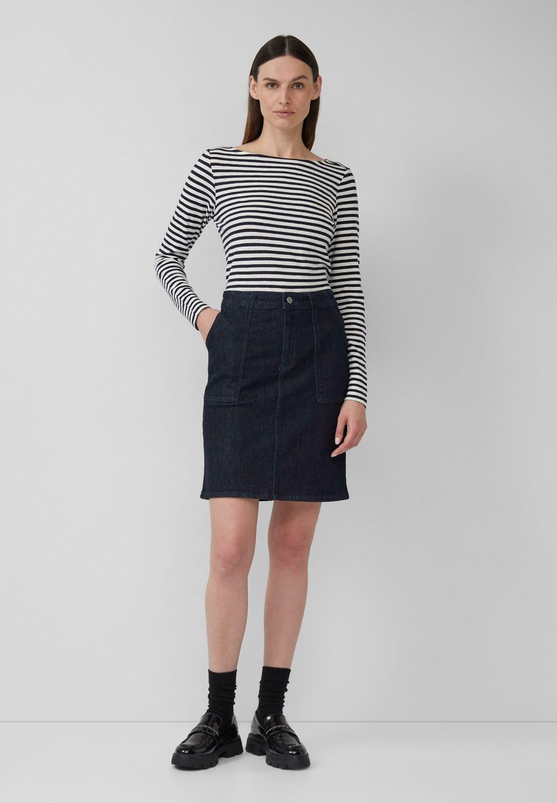 Un haut à manches longues rayé en noir et blanc, associé à une jupe crayon en denim foncé avec poches avant et fermeture par bouton, portée avec des chaussures noires.