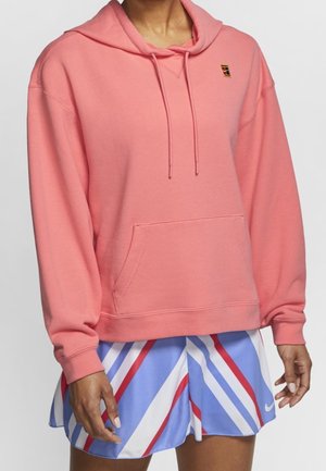 Person wearing a pink hooded sweatshirt with a front pocket and multicolored striped athletic skirt with red, white, and blue diagonal lines.