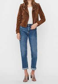 Hnědá suede motorkářská bunda s detaily na zip, kombinovaná s modrými džíny s ohrnutými manžetami a muly na podpatku s hadím vzorem. Pod ní bílý tričko.