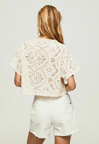 Haut cropped blanc avec des motifs découpés floraux et des manches courtes, assorti de shorts blancs effilochés. Tissu léger et design décontracté.