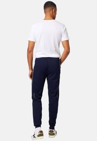 Sudaderas navy con cinturilla elástica, puños acanalados y rayas blancas a los lados. Combinadas con una camiseta básica blanca de cuello redondo y zapatillas casuales.