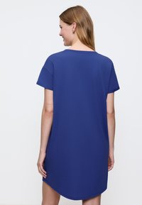 Niebieska sukienka w kształcie koszulki z krótkimi rękawami, okrągłym dekoltem i zakrzywionym dołem. Wykonana z miękkiej tkaniny; charakteryzuje się luźnym krojem i minimalistycznymi zdobieniami.