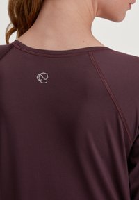 Bordeaux lange mouw top met een soepele textuur, raglanmouwen en een klein logo op de bovenrug.