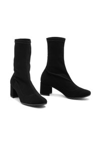 Botas de tobillo de tela negra con punta afilada y tacón ancho. El diseño presenta detalles de costura y una textura suave en toda la superficie.