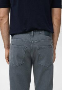 Grå denim jeans set bagfra, med standardlommer, bæltestrop og en glat tekstur. Linningen er mørkeblå.