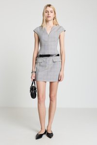 Graues kariertes tailliertes Kleid mit Kapuzenärmeln, V-Ausschnitt und Fronttaschen. Akzentuiert mit einem schwarzen Gürtel und kombiniert mit schwarzen spitzen Ballerinas und einer Handtasche.