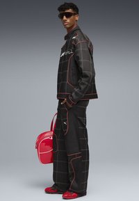 Black and red checkered jacket and pants, with white accents. Glossy red bag. Sleek black shoes, modern sunglasses.