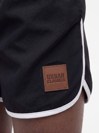 Schwarze Shorts mit weißem Besatz und einem braunen Lederpatch mit der Aufschrift "Urban Classics" am linken Oberschenkel.