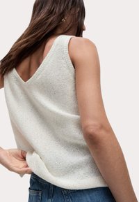 Stickad linne i off-white med V-rygg, med en lös passform och texturerad tyg. Sömmen faller nedanför midjan, i kombination med blå denim.