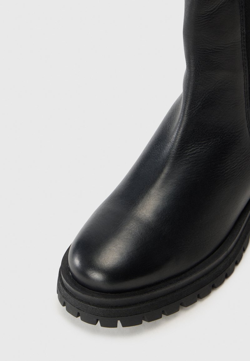 Schwarze Lederstiefel bis zum Knöchel mit runder Zehenpartie, strukturiertem Obermaterial und einer dicken, rillenartigen schwarzen Sohle für bessere Traktion.