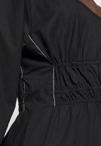 Svart klänning med samlad midja med elastik och vita söm detaljer. Slätt tyg med en åtsittande design och rundad halsringning.