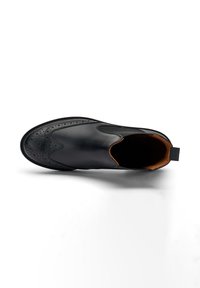 Zapato negro de cuero tipo slip-on con detalles decorativos de brogue, forro de cuero marrón claro y diseño de punta redondeada. Minimalista con líneas limpias.