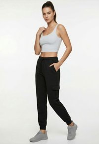 Schwarze Jogginghosen mit Kordelzug an der Taille und Seitentaschen, kombiniert mit einem grauen Crop-Top. Strukturierter Stoff und figurbetonte Silhouette. Graue Sneakers vervollständigen das Outfit.