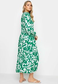 Langärmliges Kleid mit grün-weißer Musterung, das einen gestuften Rock und eine lockere Passform aufweist. Der Stoff sieht leicht aus und hat eine subtile Textur.