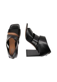 Schwarze Leder Absatzsandalen mit quadratischer Zehenpartie, ausgestattet mit kreuzenden Riemen und einem massiven geometrischen Absatz. Die Innenseite hat eine glatte, sandfarbene Textur.