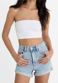 Top blanco sin tirantes combinado con shorts de denim azul claro de cintura alta, que presentan puños enrollados y una cintura con botones.