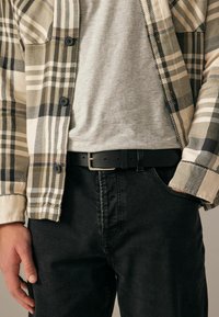 Koszula w kratę w kolorze kremowym, zielonym i czarnym, w połączeniu z szarym T-shirtem i czarnymi dżinsami. Posiada guziki oraz czarny pasek z srebrną klamrą.