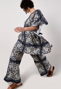 Vielseitiges Outfit in Marineblau und Creme mit einer lockeren Bluse und weiten Hosen, gefertigt aus leichtem Stoff. Braune Sling-Sandalen.